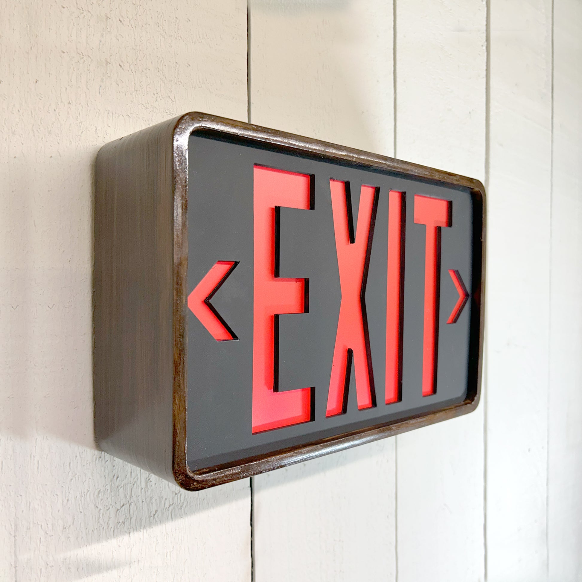 Eames inspired bent wood exit sign with red letters on a white background, mounted on a wall.