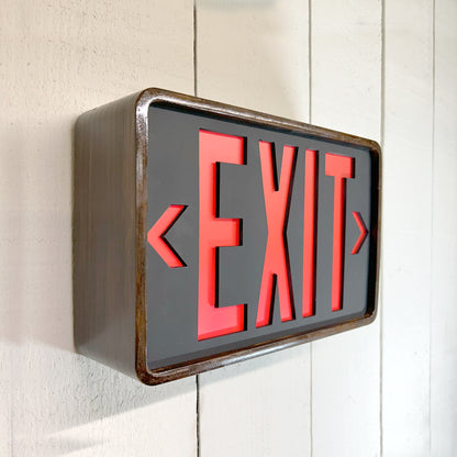 Eames inspired bent wood exit sign with red letters on a white background, mounted on a wall.